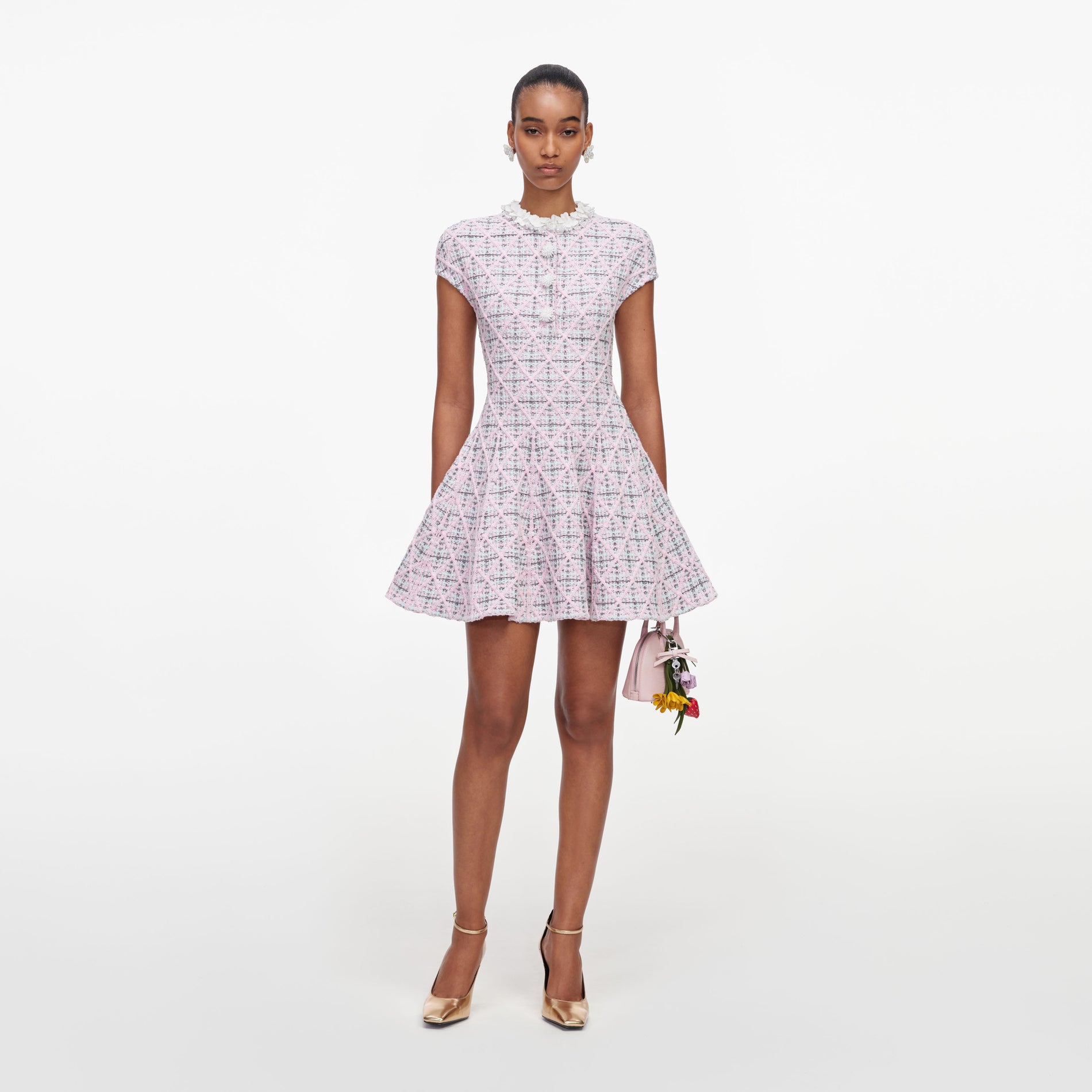 Model wearing a pink tweed dress with a ruffled collar, gold heels, and a pink handbag with floral charms