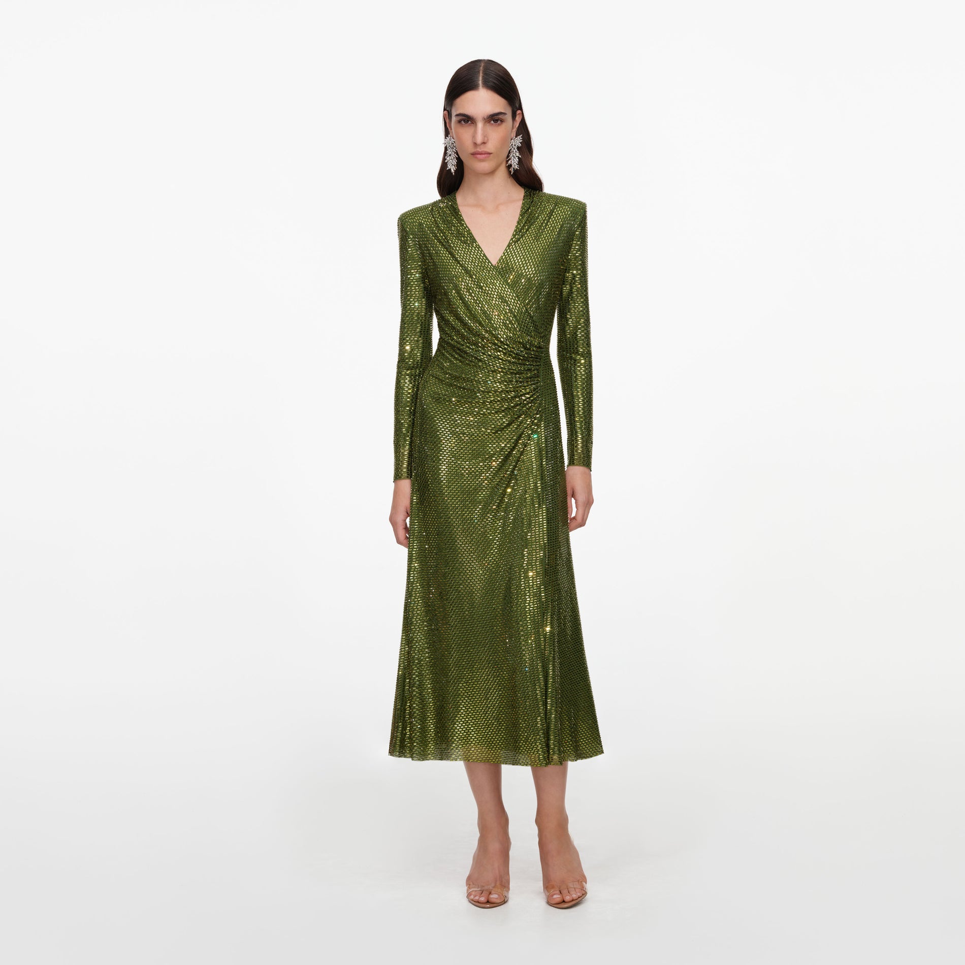 Woman in a long-sleeved, v-neck, wrap-style green sequin dress with pointed shoulders and clear heels