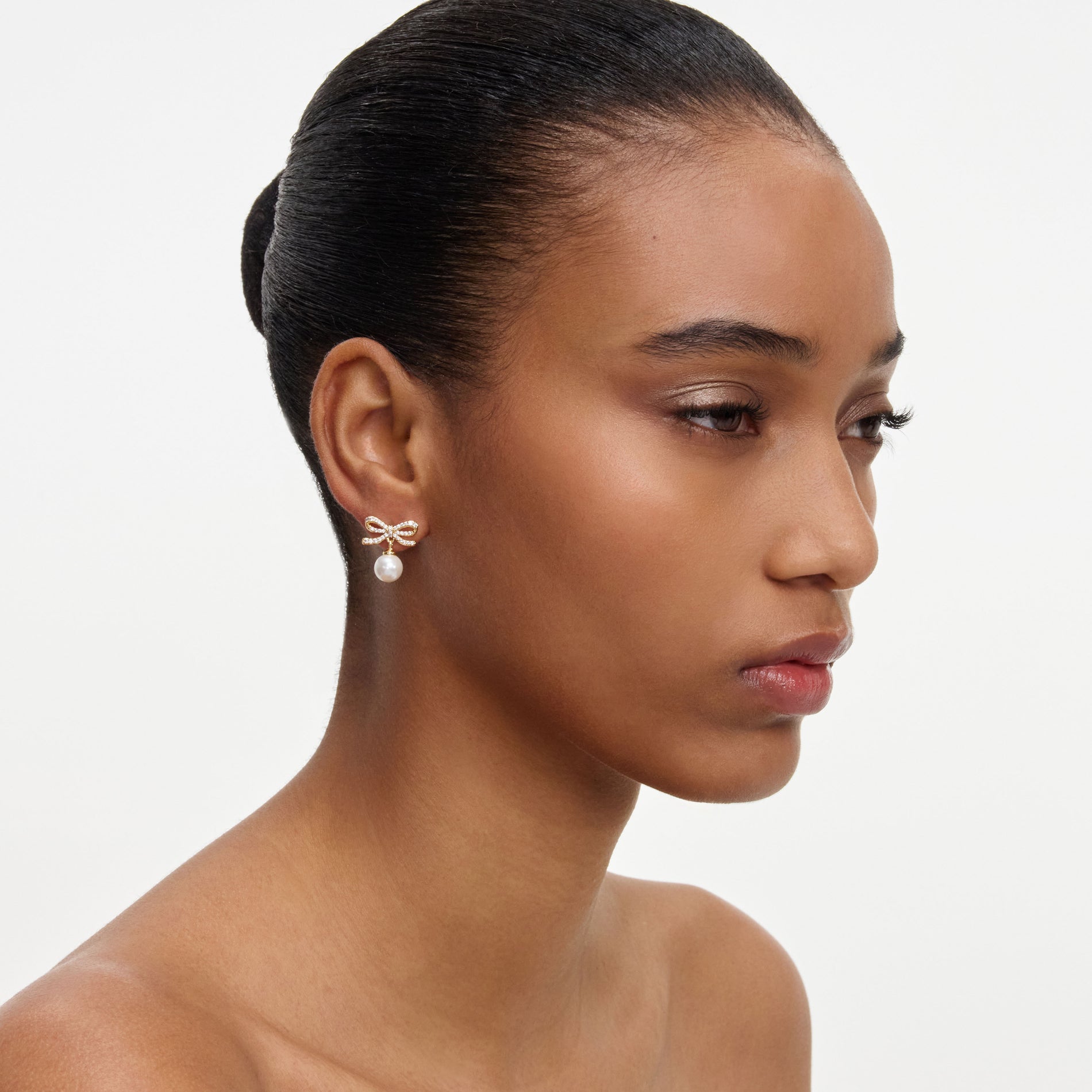 A close up of a woman wearing the Gold Bow Pearl Earrings