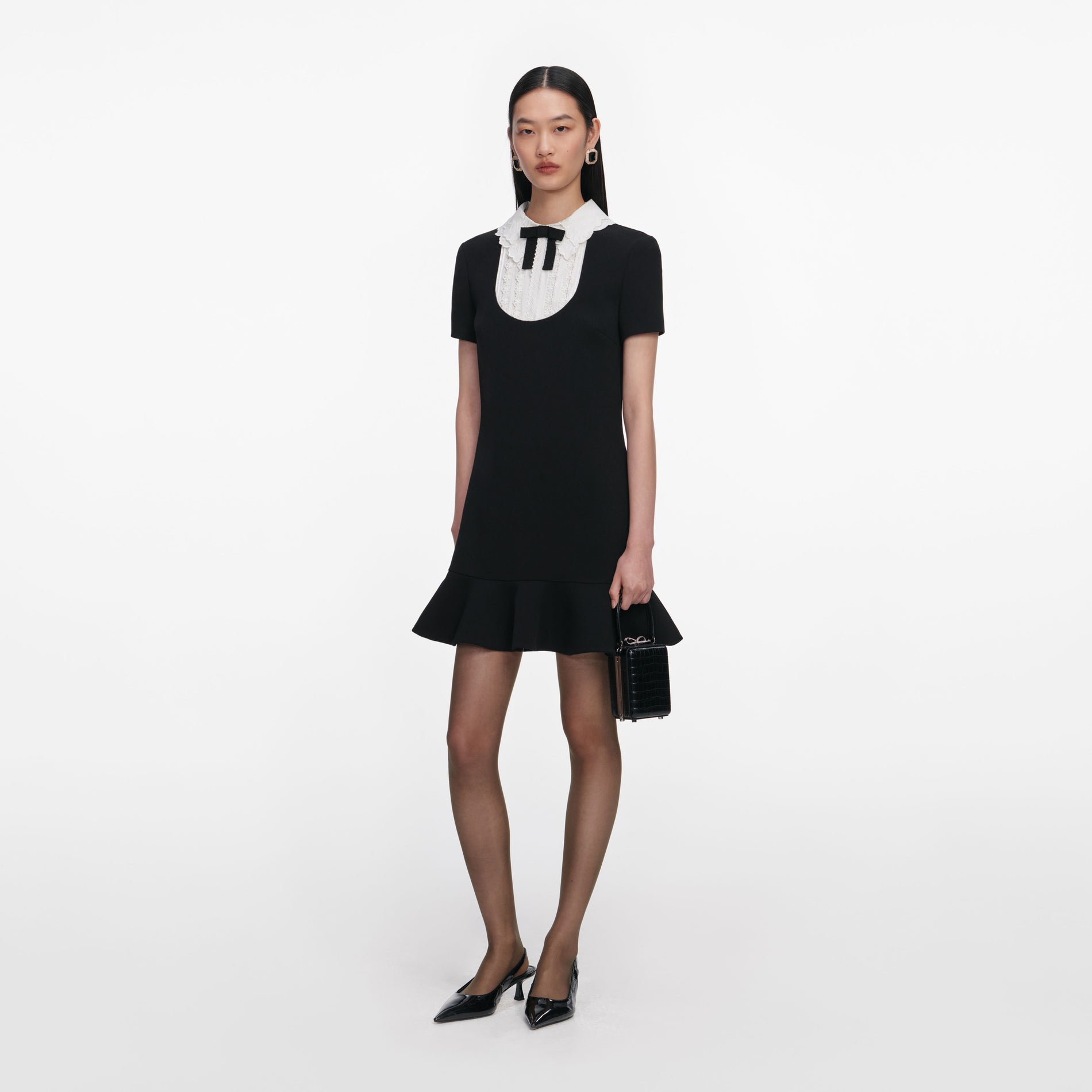 Side view of a woman wearing the Black Crepe Lace Bib Mini Dress