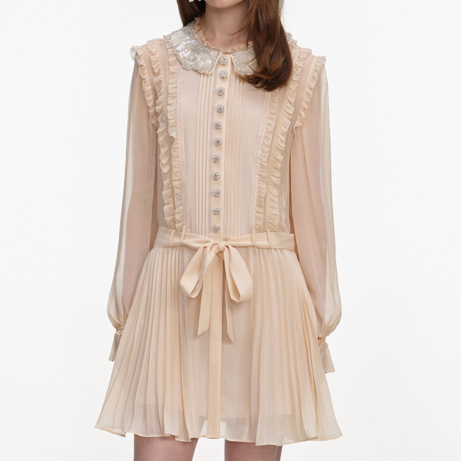 A close up of a woman wearing the Tan Pleated Georgette Mini Dress